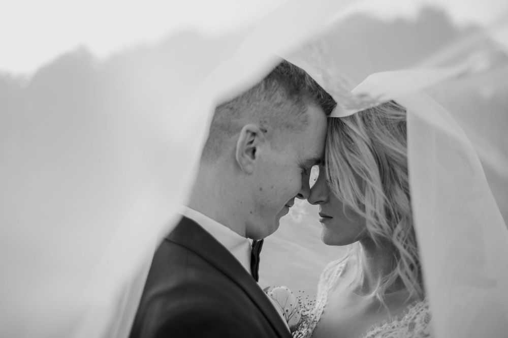Black and white intimate portrait of newlyweds under bridal veil.