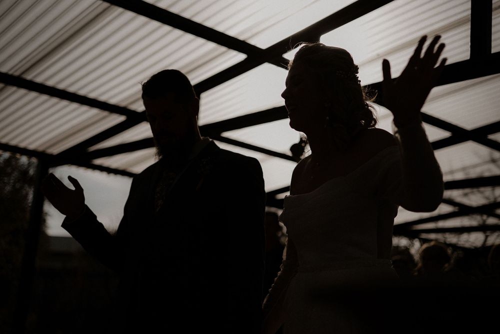 Silhouettes of people dancing under an outdoor pergola structure.