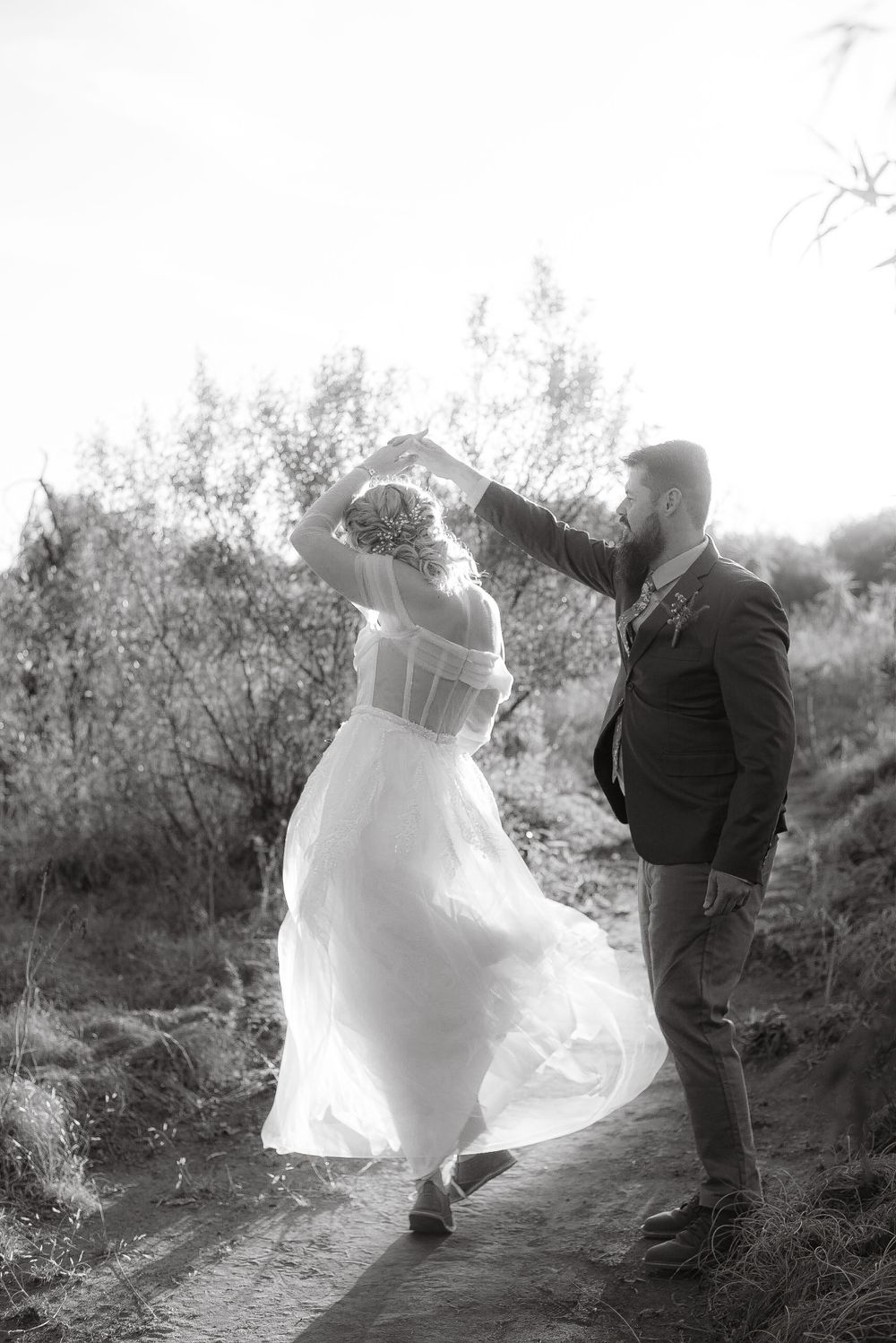 A black and white dancing photo showing movement with a flowing wedding dress in an outdoor setting.