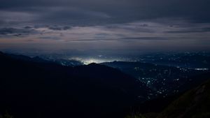 Nighttime cityscape nestled in a valley with mountain silhouettes and twinkling lights.