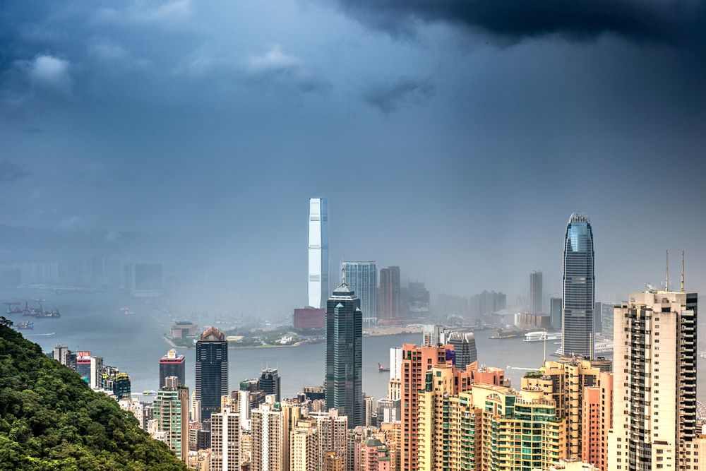 Dramatická panoráma Hongkongu s výškovými budovami v hmle a tmavých búrkových oblakoch, kontrast prírody a mesta.