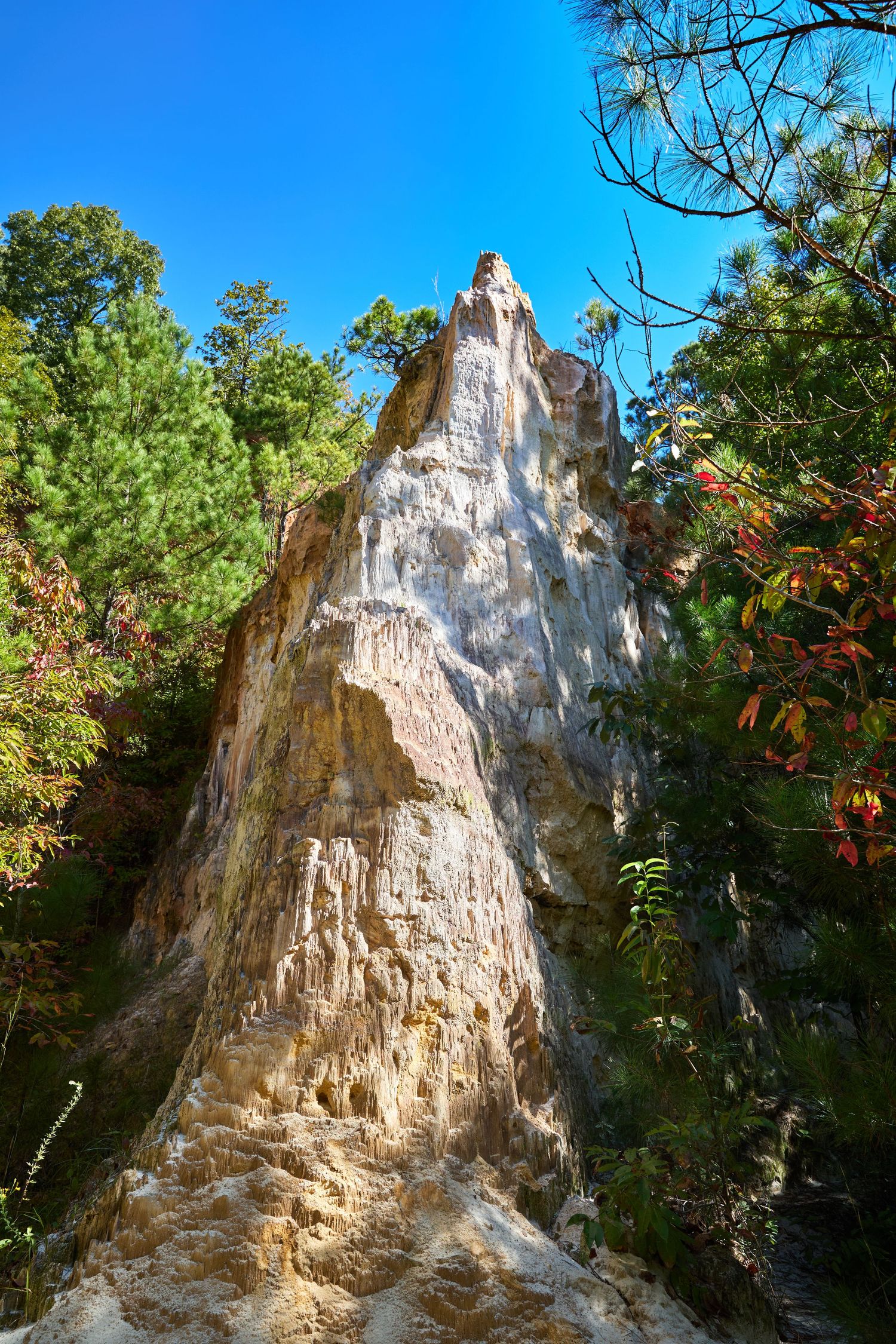 Towering white limestone formation rises against bright blue sky surrounded by green trees and autumn foliage.