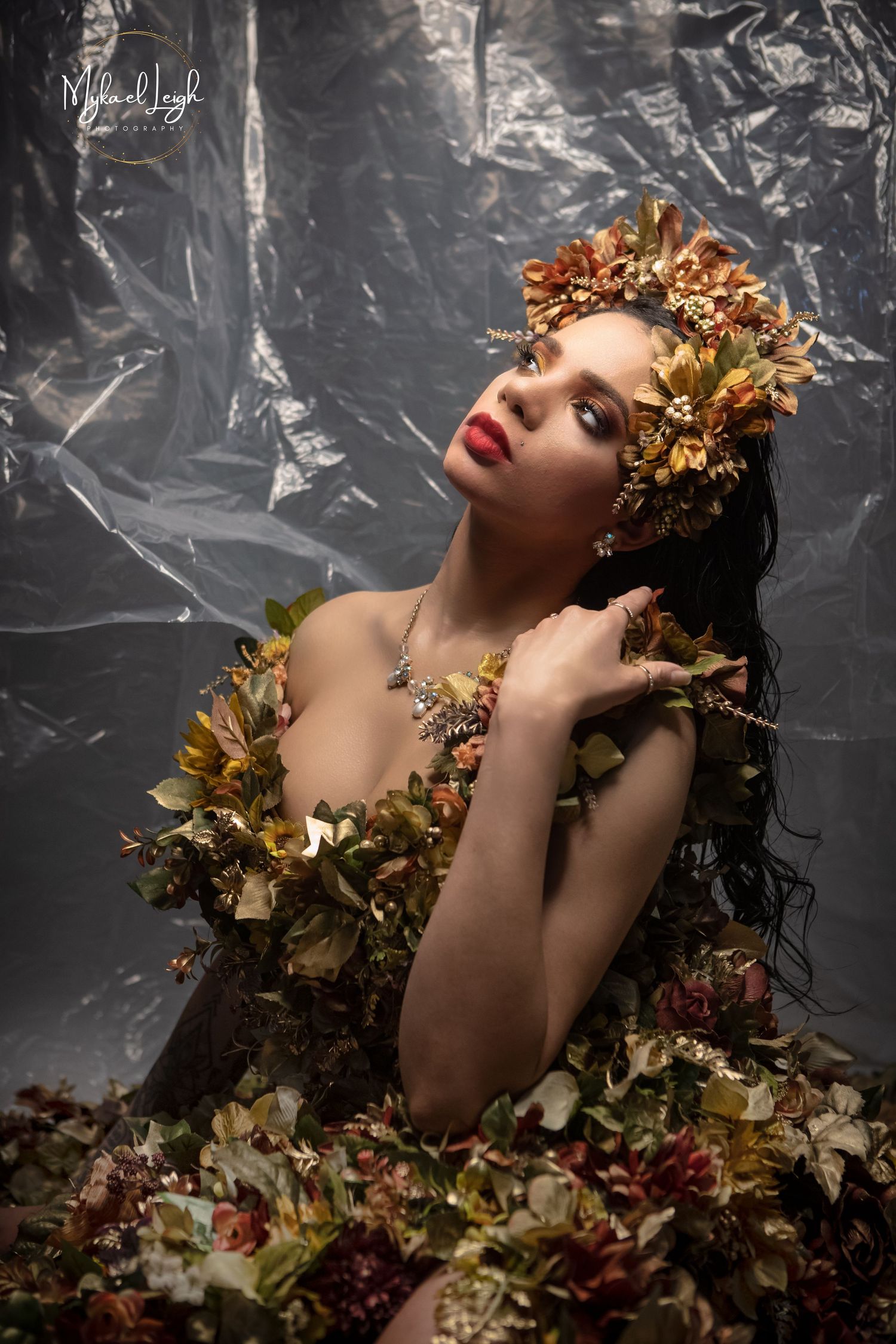 Dramatic fashion portrait with golden floral crown against metallic background.