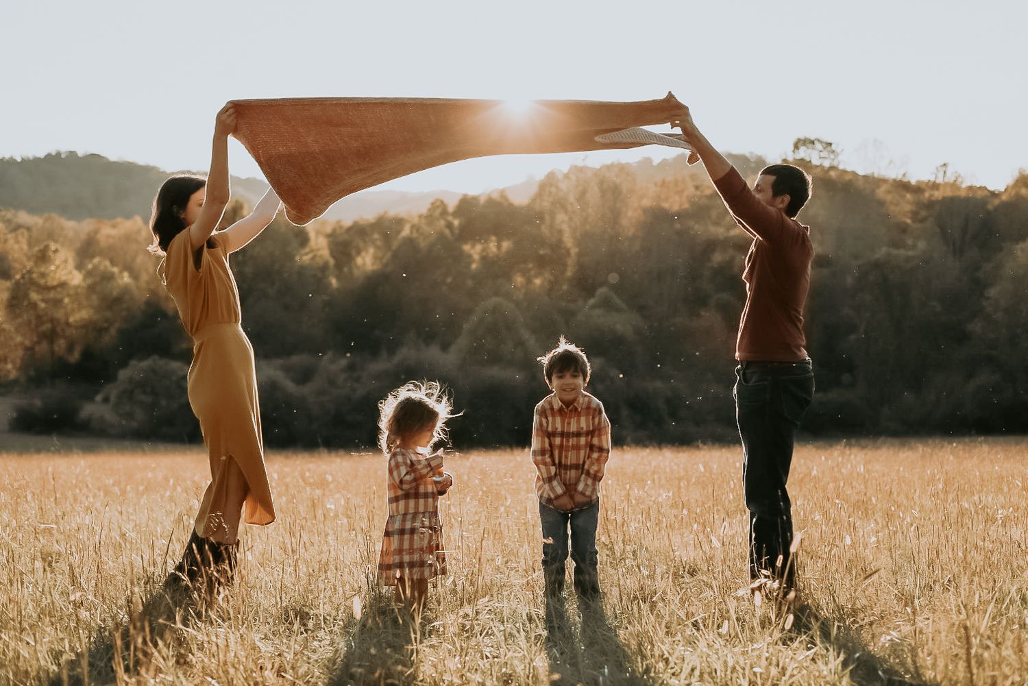Family holding up blanket together in golden sunlit field.