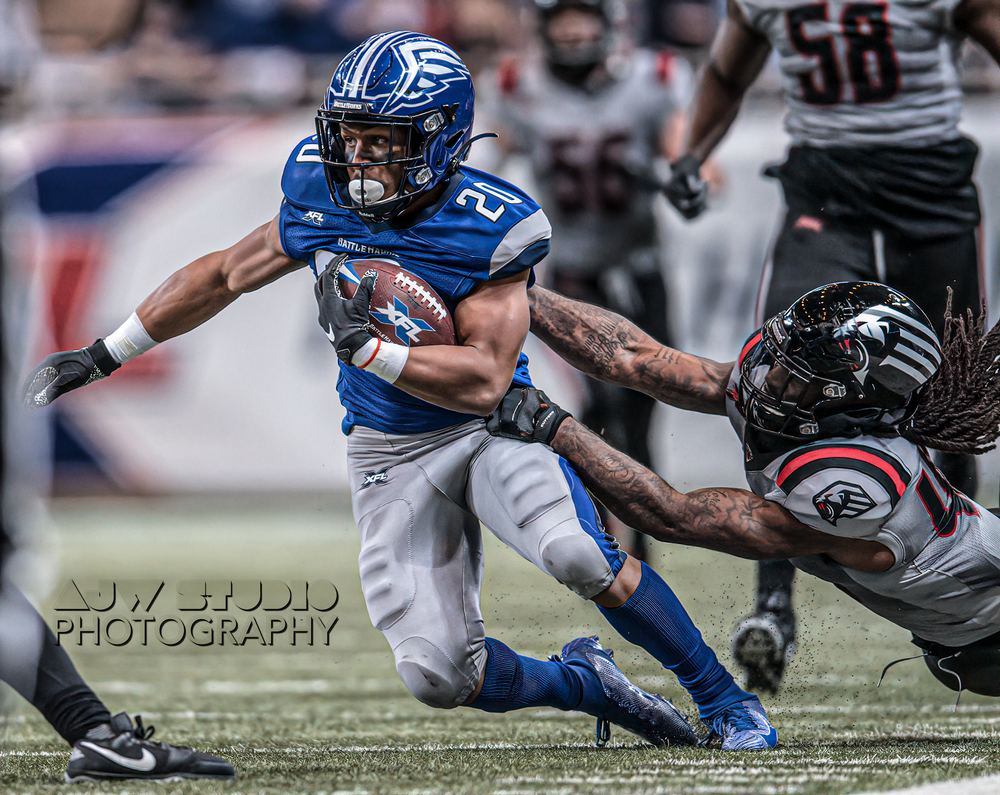 Football player in blue jersey evading tackle during intense game action.
