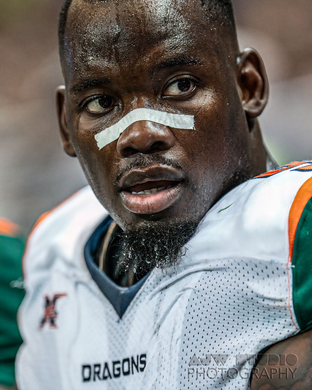 Football player in Dragons uniform with athletic tape on nose during game.