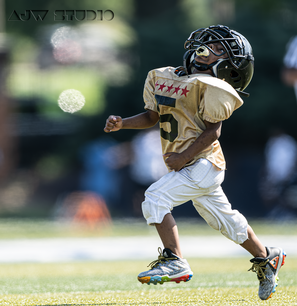 Young player in tan uniform runs with determination during youth football game.