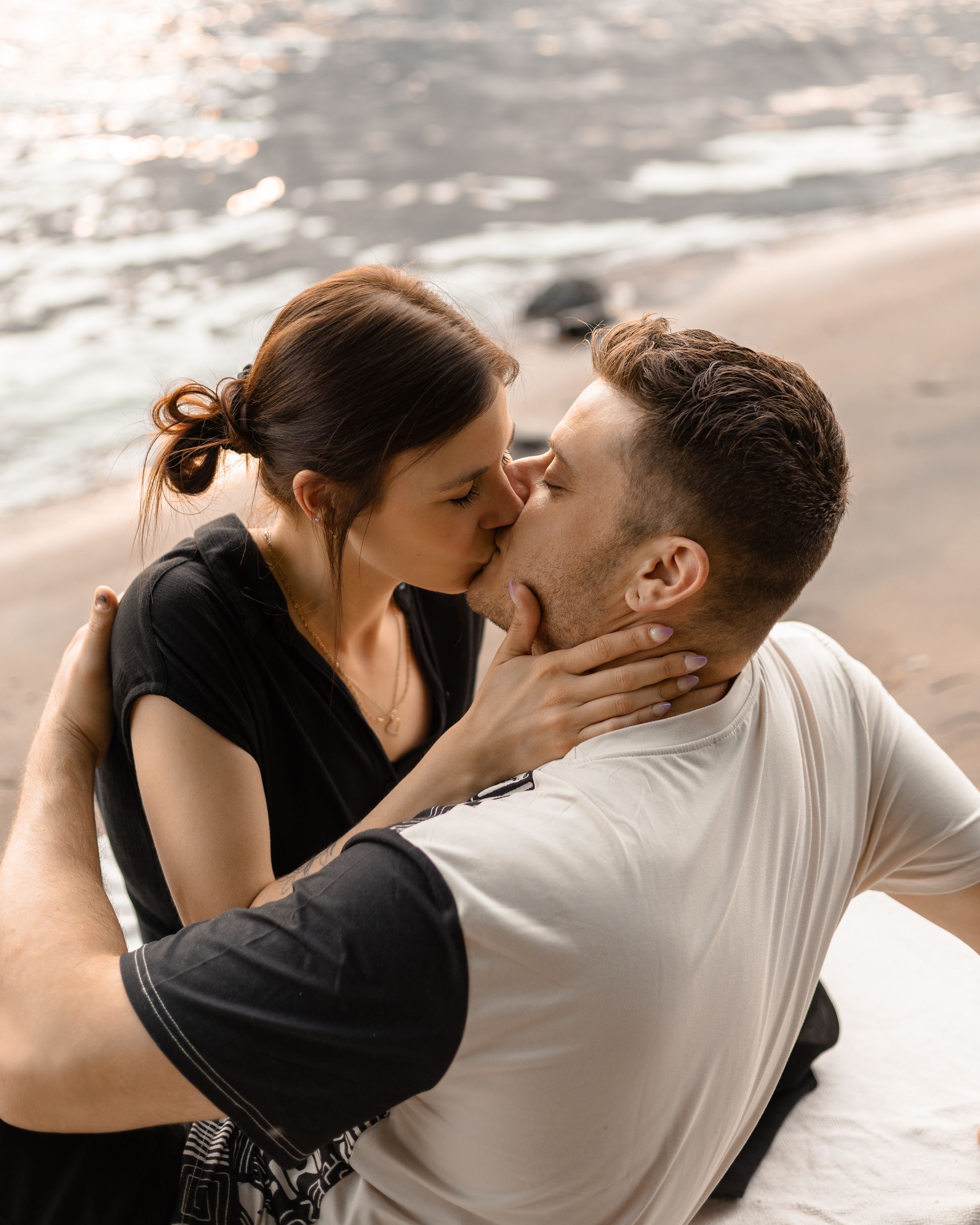Intimate beach moment with couple in black and white clothing against ocean backdrop.