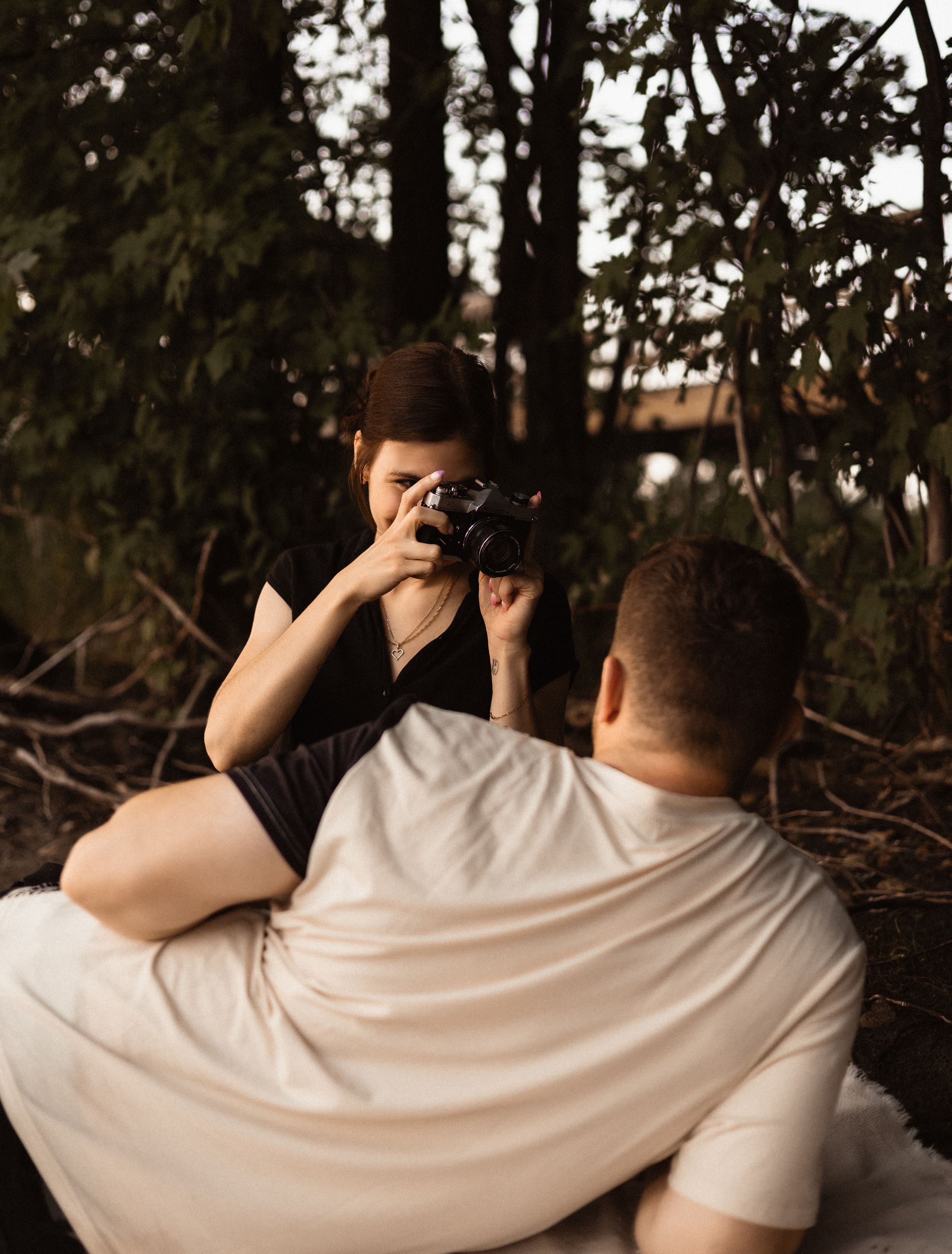Person taking photo with camera while sitting in nature during golden hour.