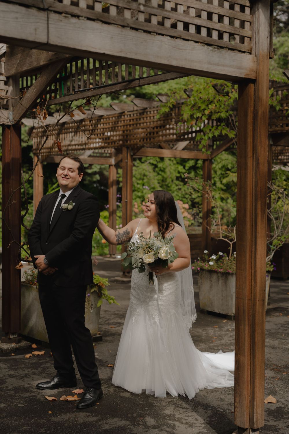 Wedding couple shares joyful first look moment under garden pergola.