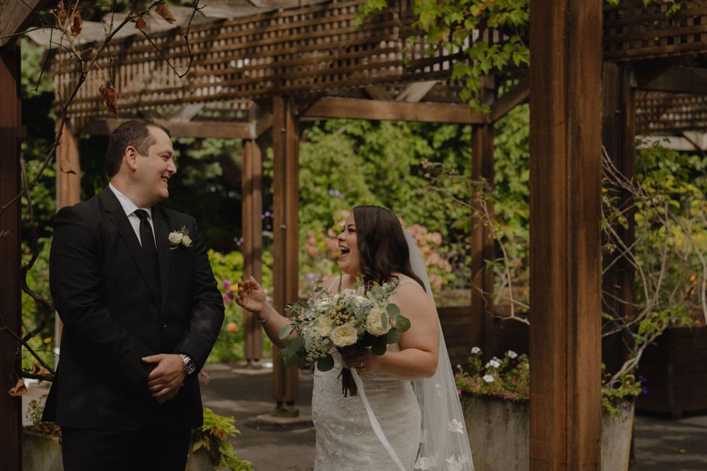 Couple shares candid moment under wooden pergola during wedding first look.