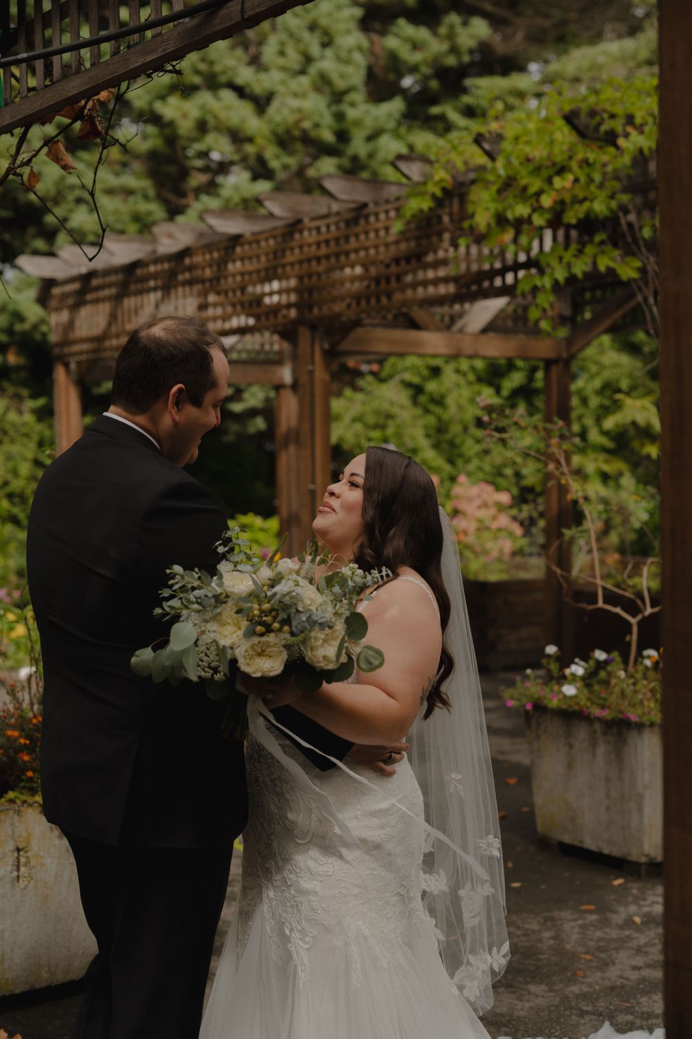Romantic first look between couple under rustic garden pergola with floral details.