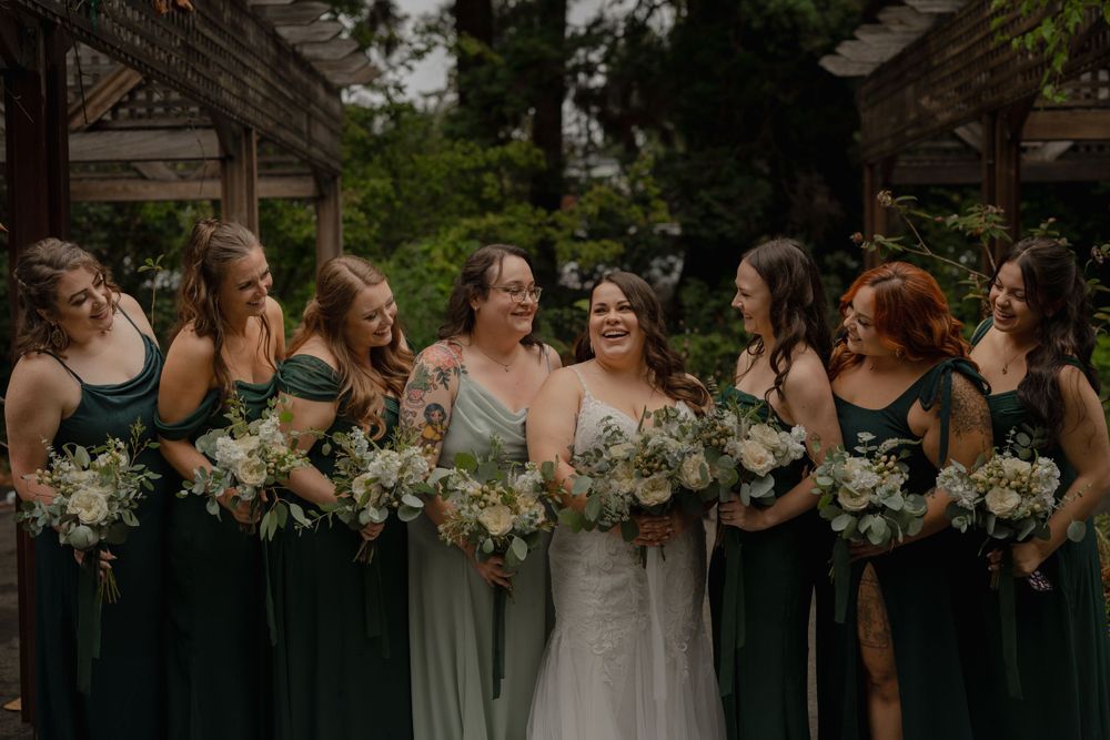 Bridesmaids in emerald green dresses pose with bouquets at an outdoor garden wedding.