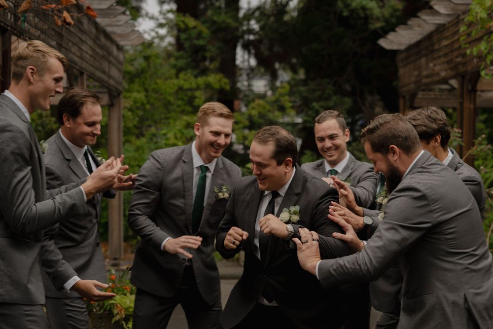 Groomsmen in gray suits share a lighthearted moment during wedding celebrations.