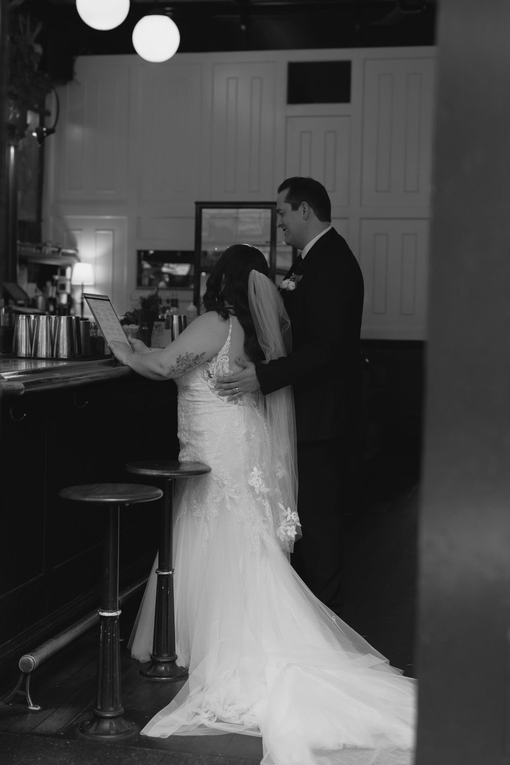 Black and white photo of a couple reading at a bar during their wedding celebration.