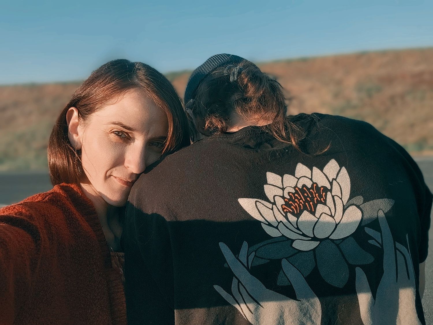 Two people at sunset with one wearing jacket featuring lotus flower design.