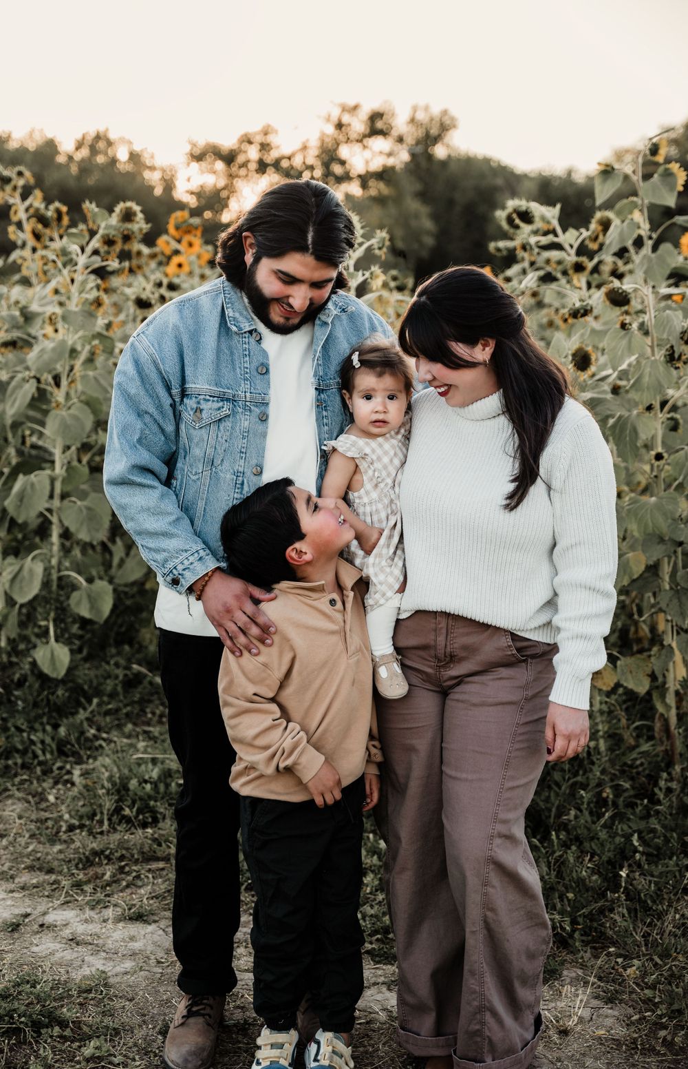 Intimate family moment captured in a golden sunflower field at dusk.