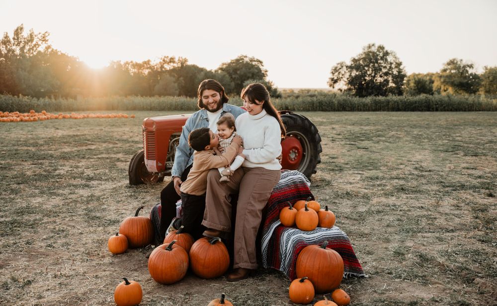 A family sits together with pumpkins in a field during golden hour sunset.