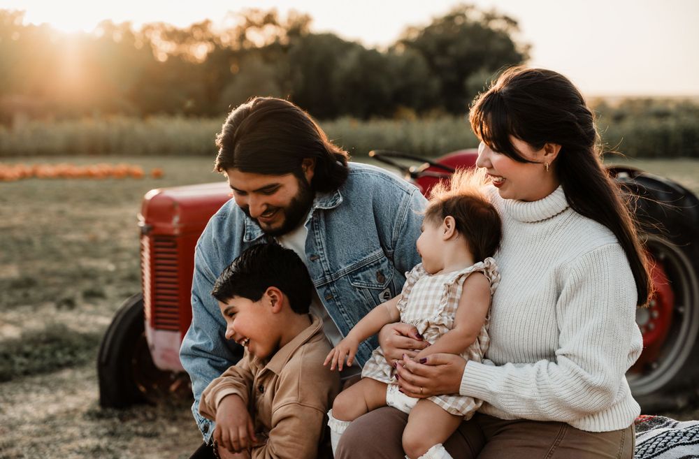 A family cuddles together on blankets near pumpkins at sunset.