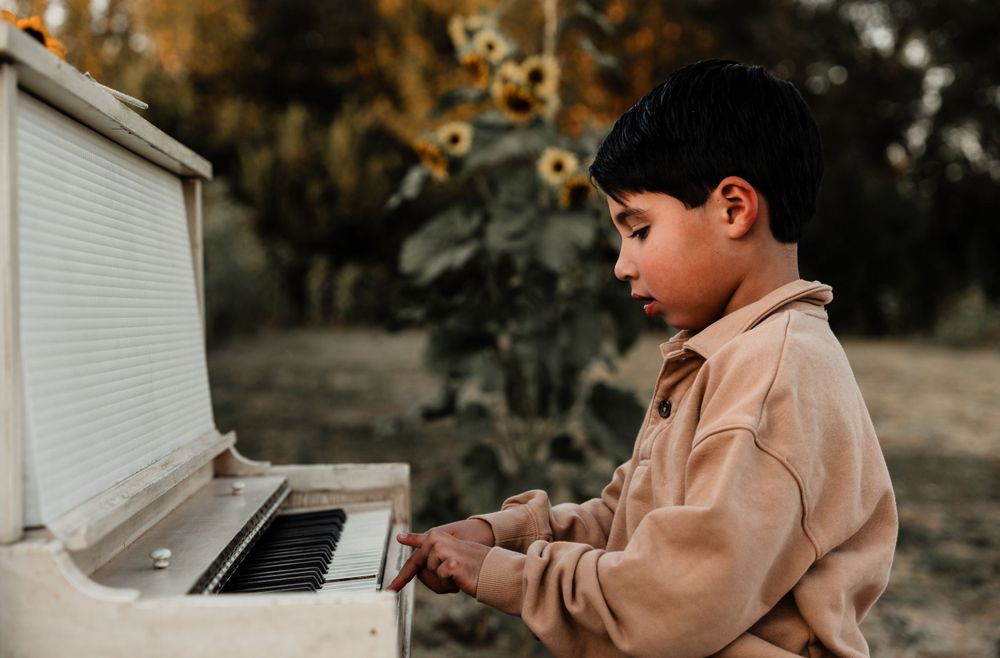 A child plays piano keys on an upright white piano outdoors.