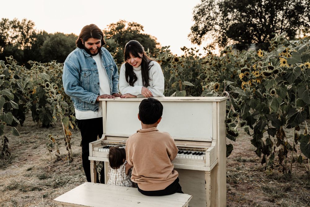 An upright white piano sits in a natural outdoor setting at sunset.