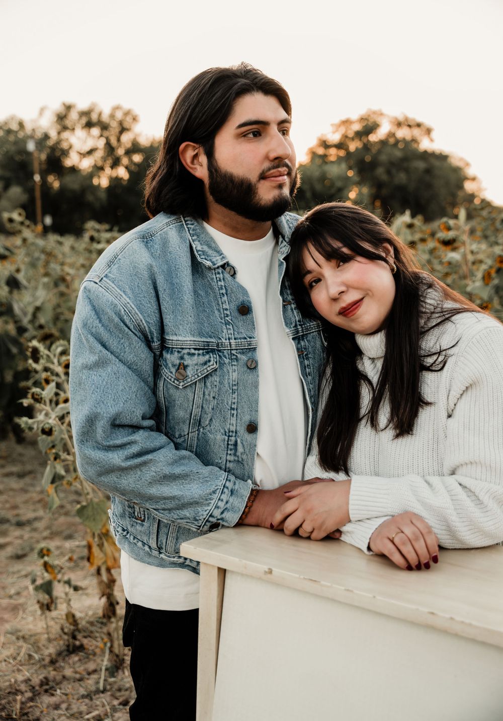 A couple shares an intimate moment leaning on a white piano outdoors.