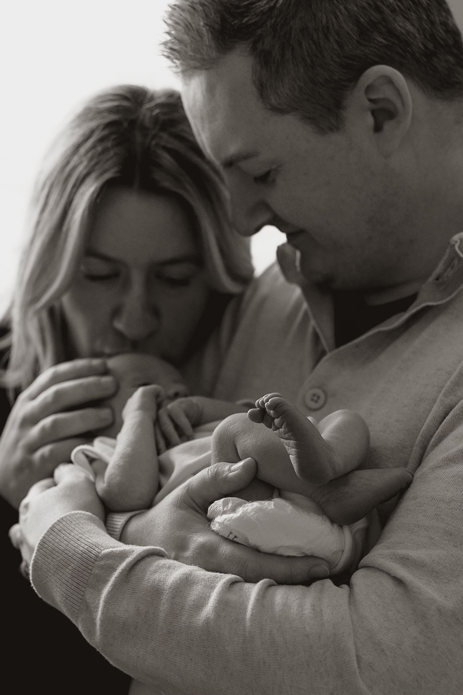 An intimate black and white portrait of new parents cradling their newborn baby.