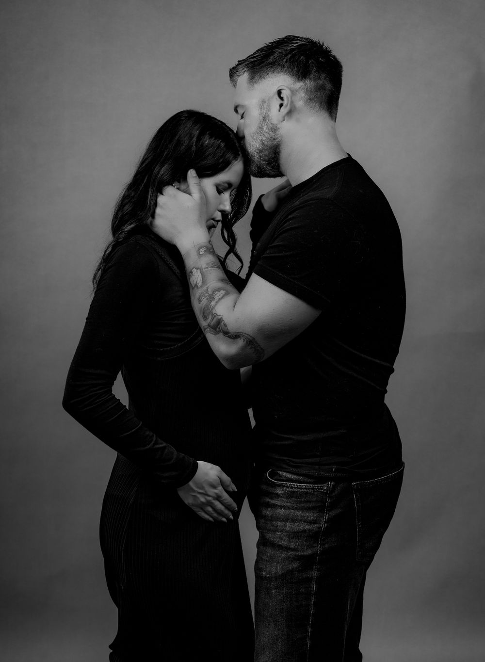 Intimate black and white photo of a couple embracing in a romantic pose against a dark background.