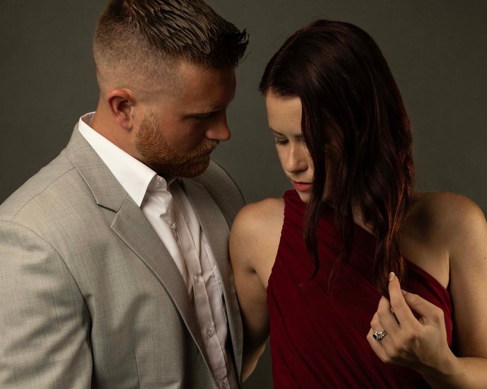 Romantic portrait of a couple in evening wear sharing a tender moment against moody lighting.