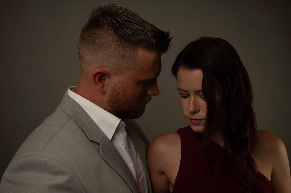 A couple in a romantic pose together, with a person in a gray suit and another wearing a maroon top.