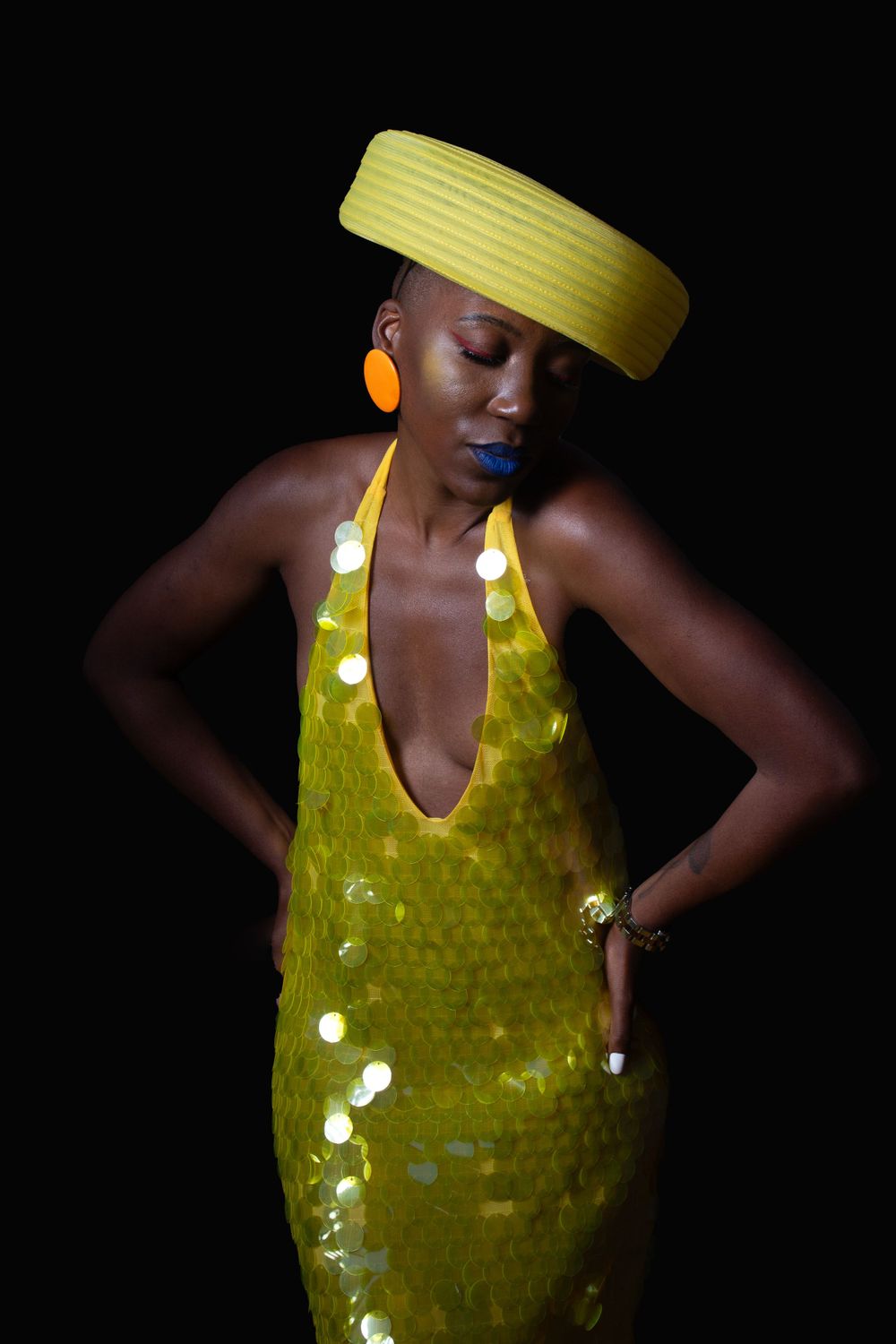 Artistic fashion portrait featuring yellow hat and sequined dress against dark background.