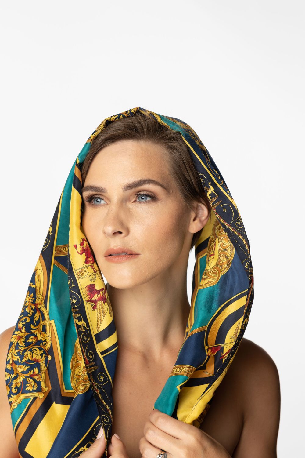 Elegant portrait with silk scarf in teal and gold baroque pattern against white background.