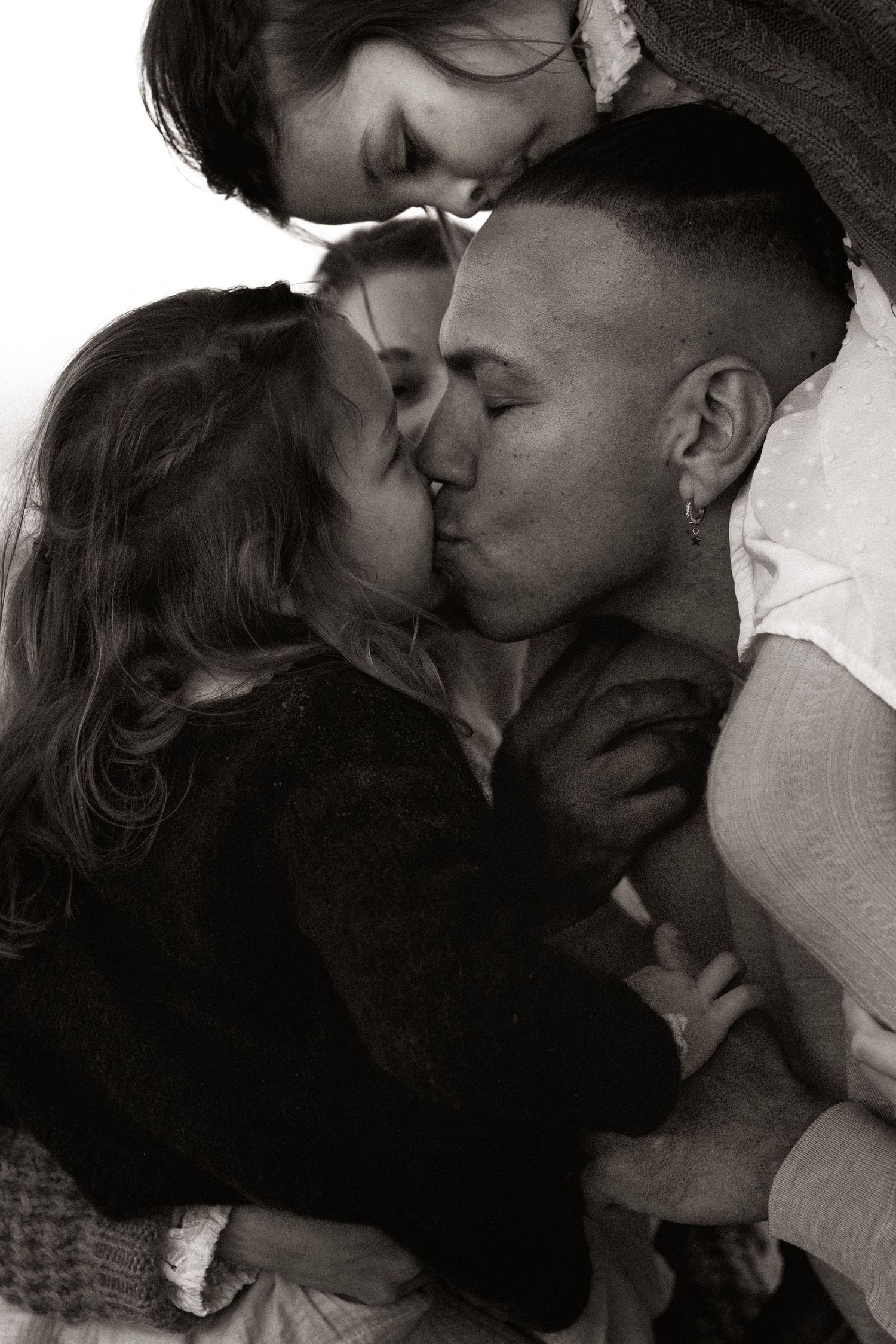 Black and white intimate close-up portrait in Denia of three people sharing a tender embrace and kiss. Denia family photographer