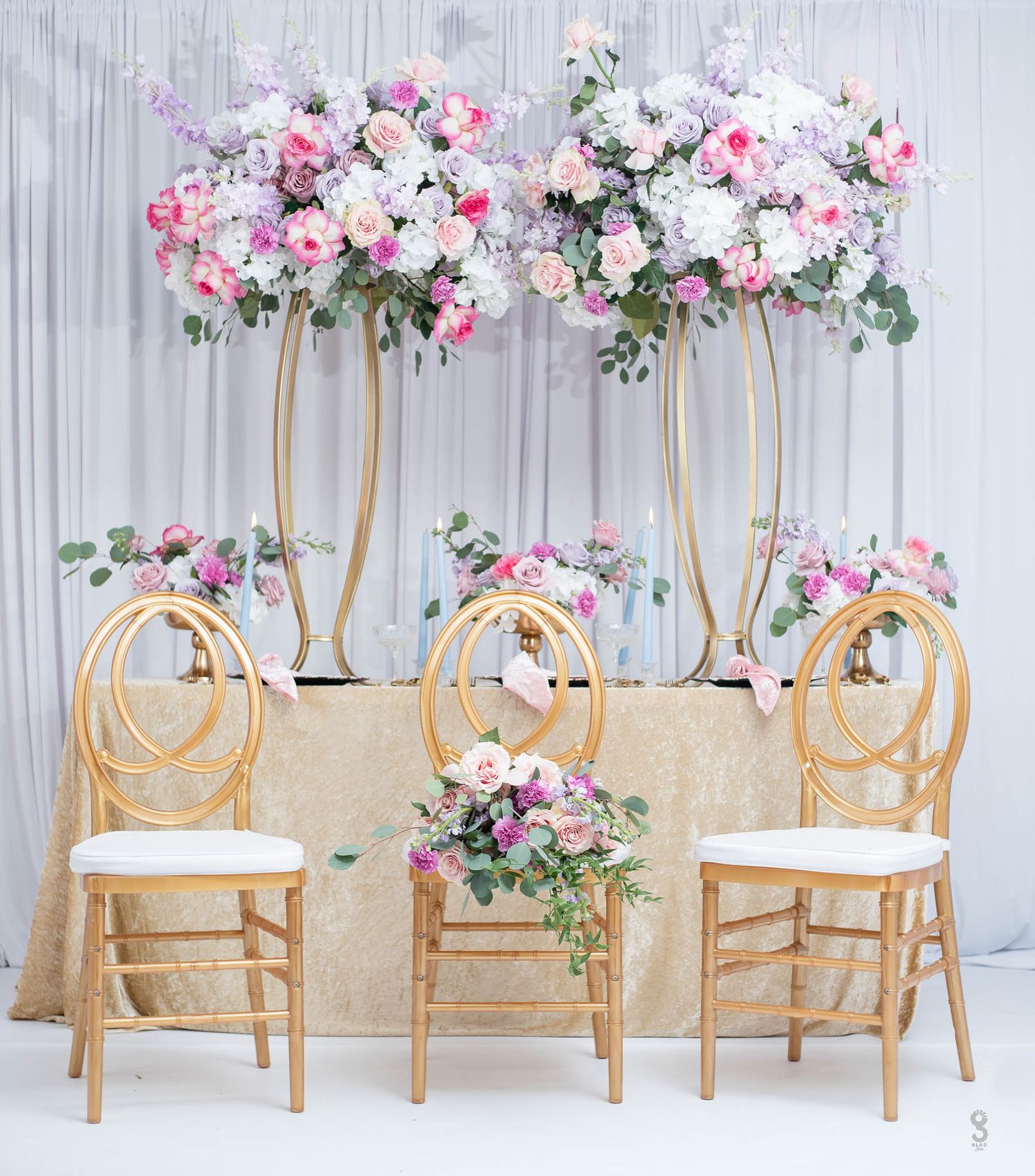 Elegant wedding decor featuring gold Phoenix chairs and tall floral arrangements in pink and white against gray backdrop. event decor photos