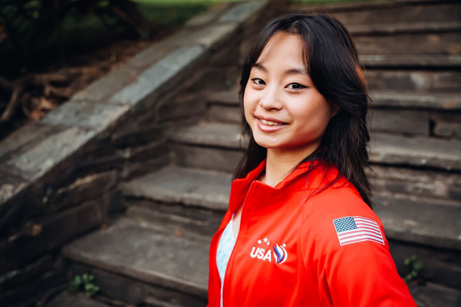 Person in bright red jacket with American flag patch posing on wooden steps.