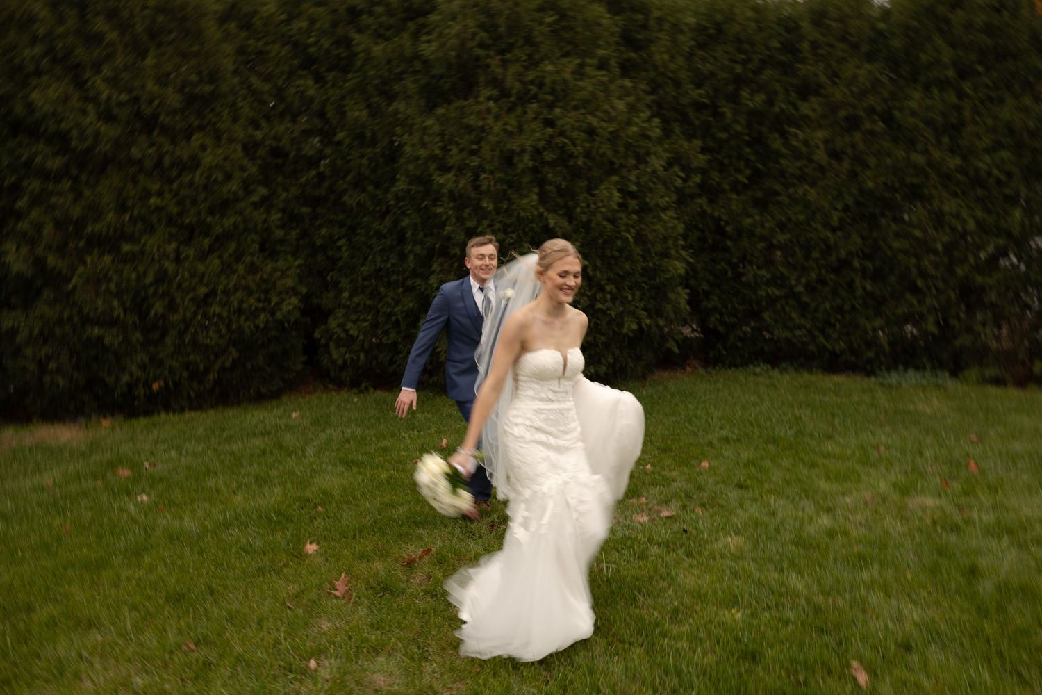 A playful wedding photo with the bride lifting her dress while walking on grass.