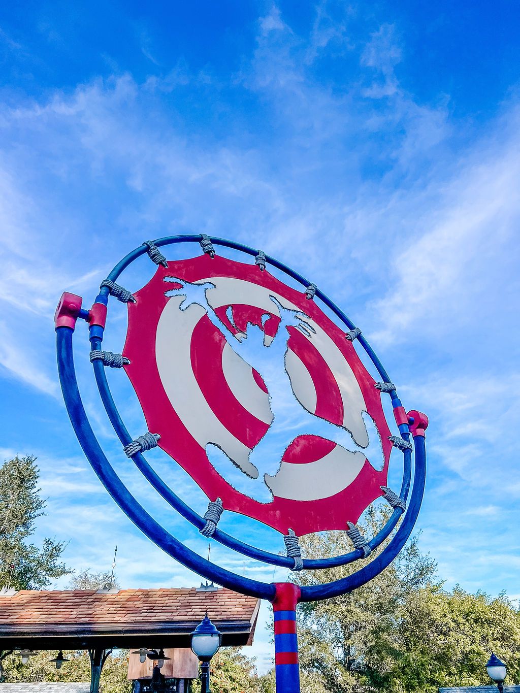 Brightly colored amusement park rides with blue and red circular designs against a vivid blue sky with wispy clouds.