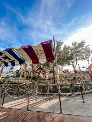 Colorful canopy awnings and rope barriers at a Disney theme park attraction entrance on a sunny day with blue skies.