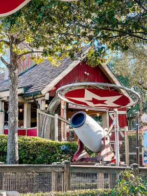 A red retro-style airplane sculpture mounted in front of a quaint house with trees and landscaping.
