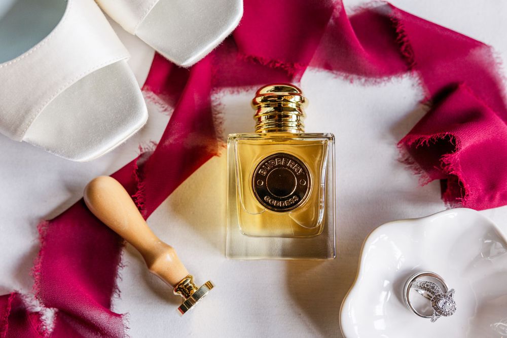 Luxury perfume bottle with golden cap placed on pink fabric alongside white accessories.