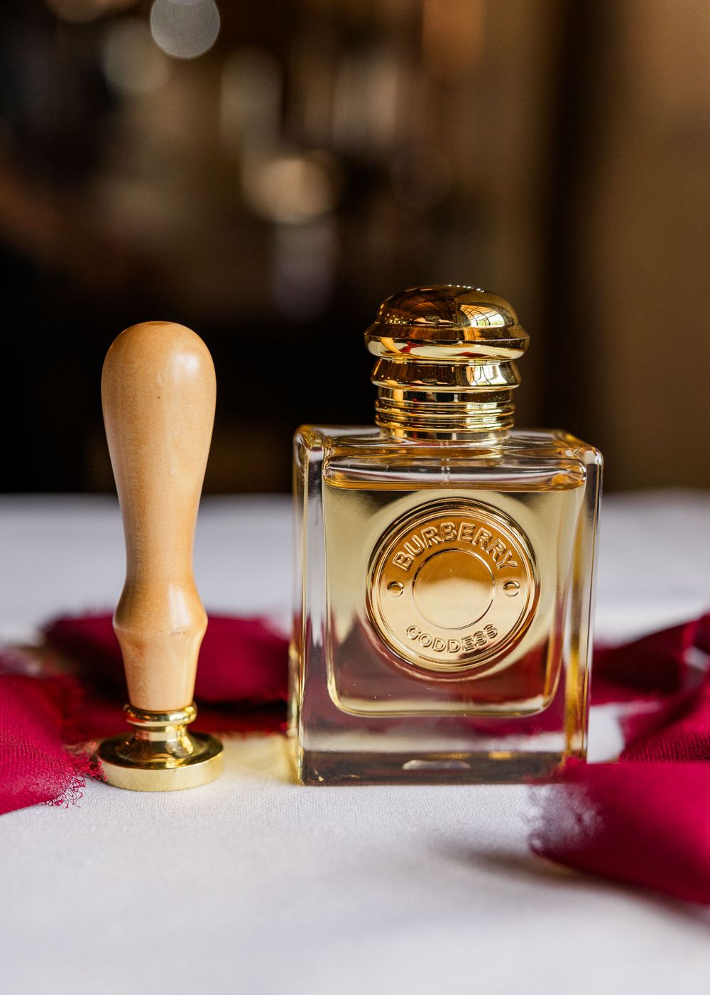 Elegant perfume bottle and wax seal stamp displayed on a red fabric background with soft bokeh lighting.