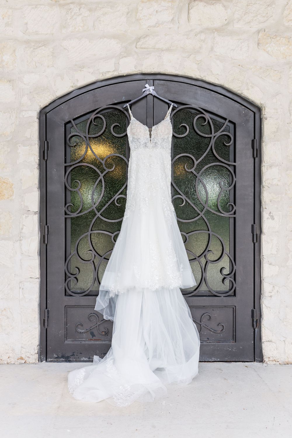 Elegant white wedding dress hanging on ornate iron door with scrollwork details and soft lighting.