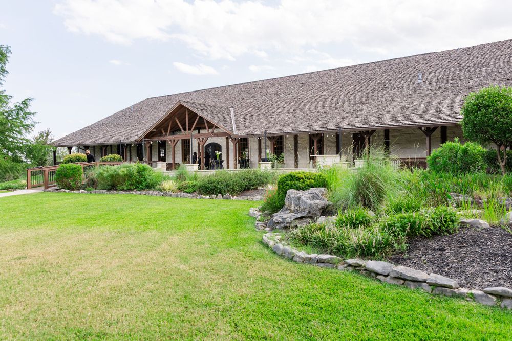Large rustic wedding venue with landscaped garden and stone pathway under cloudy sky.