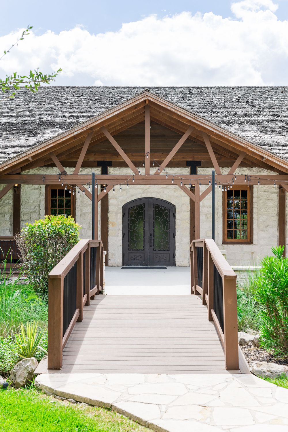 A covered wooden bridge walkway leads to an elegant stone building entrance with glass doors and timber beam accents.