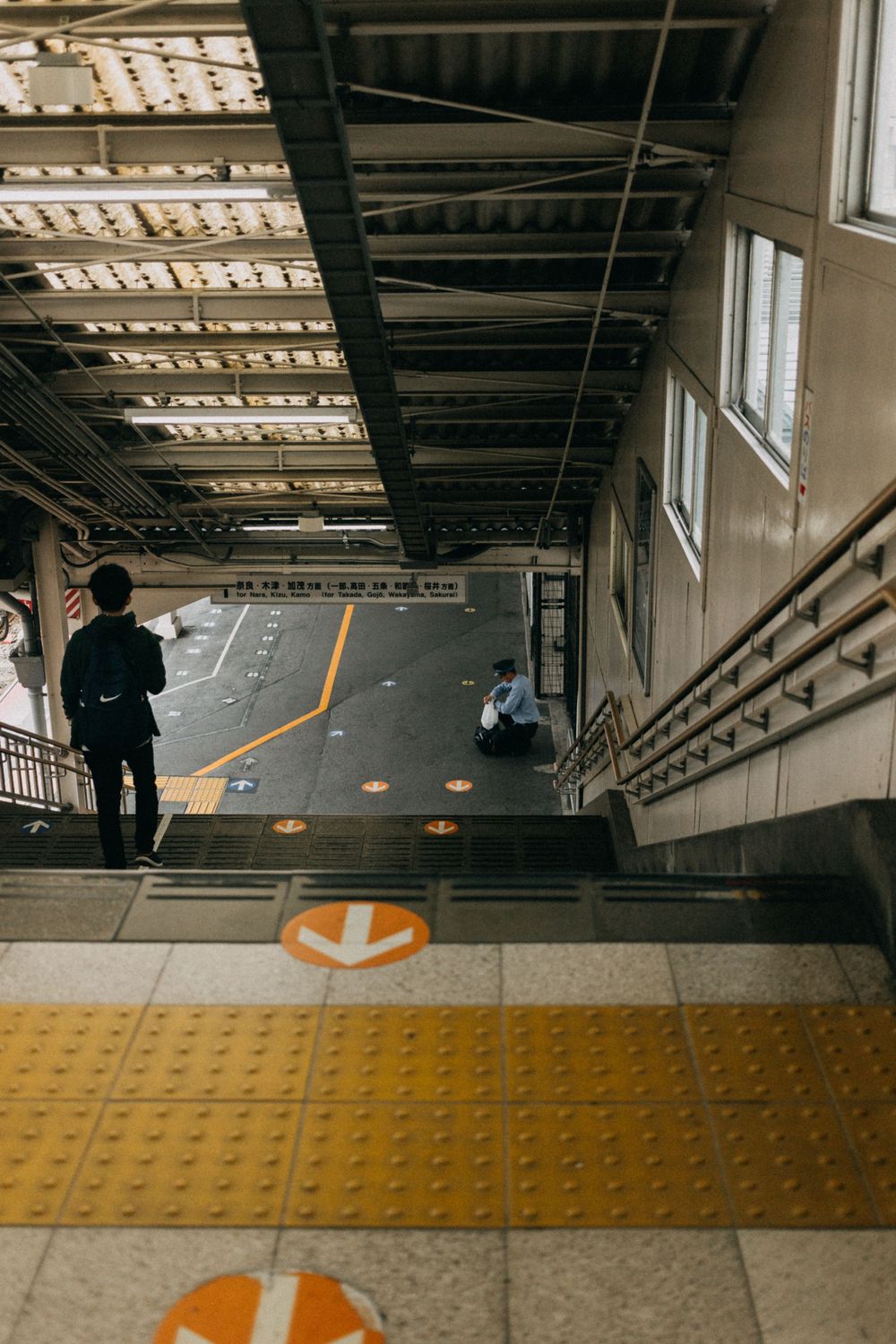 Train station interior with yellow safety markings and directional signs on the floor.