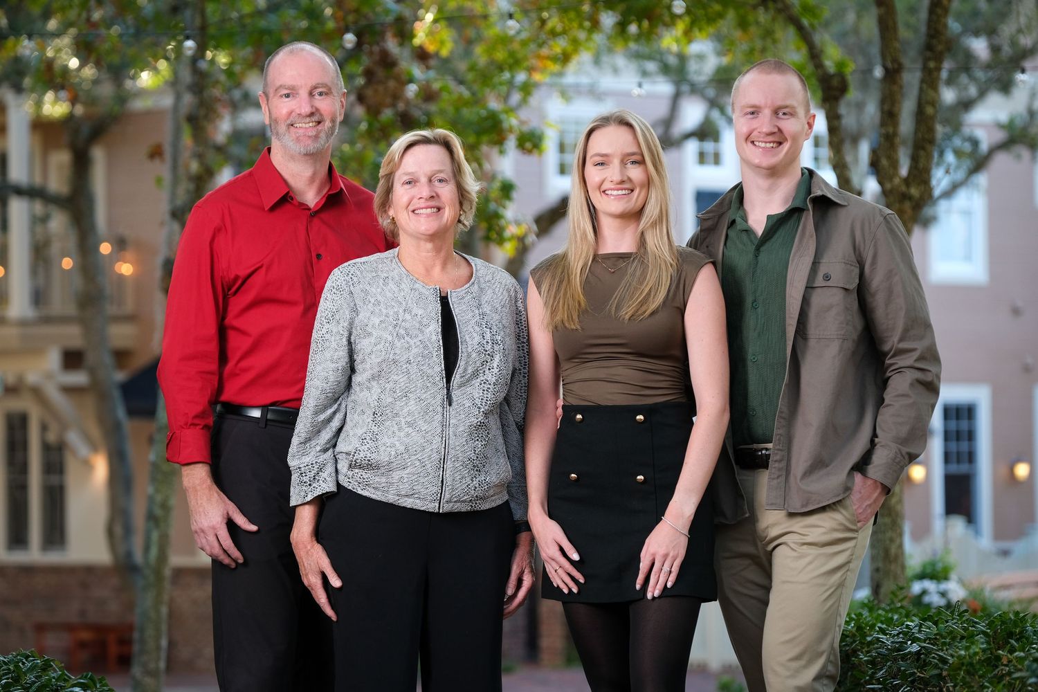 A smiling family standing together on a tree lined walkway.