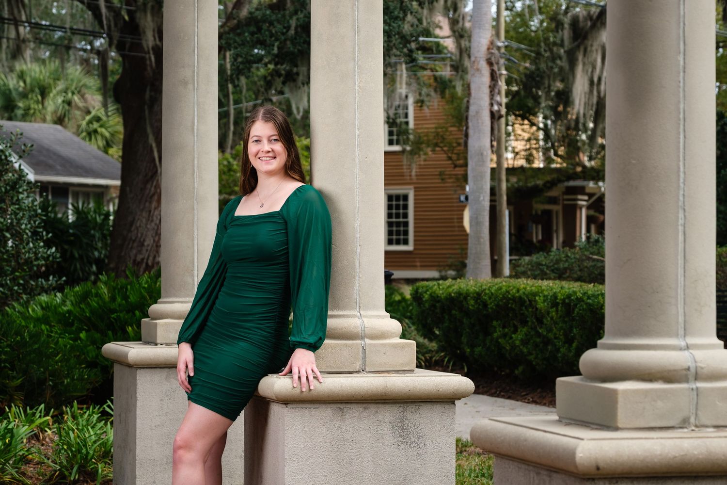 A smiling girl in a green dress leans against a decorative column.