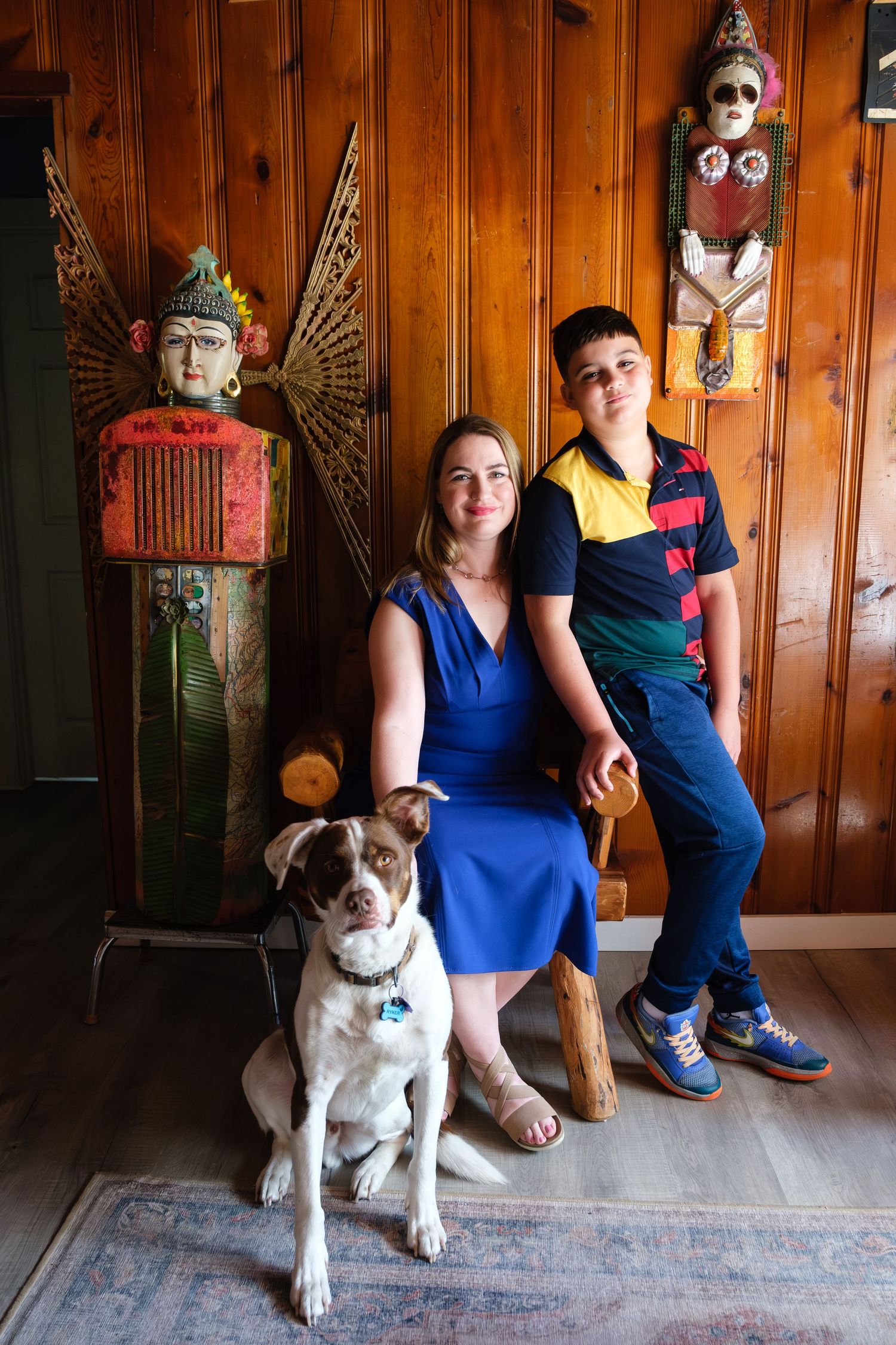 Enviromental portrait of a woman wearing a blue dress with a brown and white dog and a young boy in a yellow and red striped shirt.