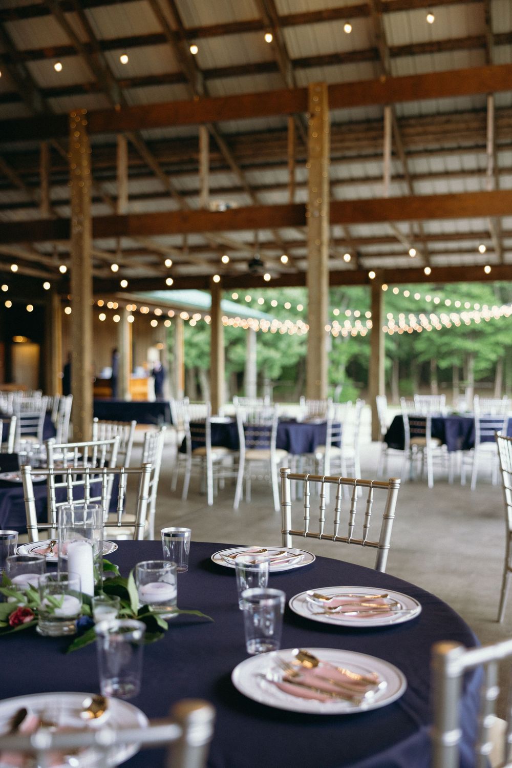 Wedding reception venue with navy tablecloths and string lights in rustic barn setting. Estate and historic venue wedding photographer NC