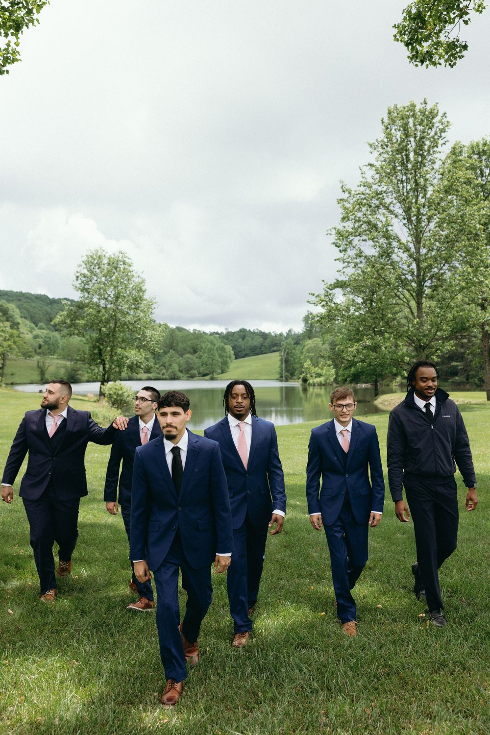Group of groomsmen walking across green lawn in navy suits. Estate and historic venue wedding photographer for NC and across the East Coast
